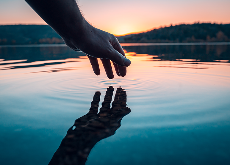 A hand touches the surface of a lake.